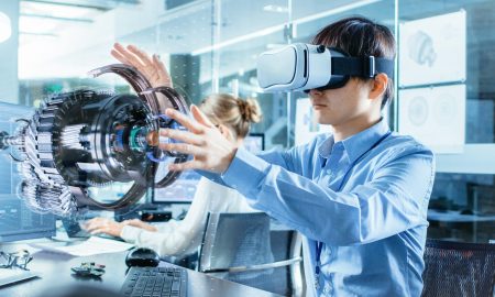 Computer Science Engineer wearing Virtual Reality Headset Works with 3D Model Hologram Visualization, Makes Gestures. In the Background Engineering Bureau with Busy Coworkers.